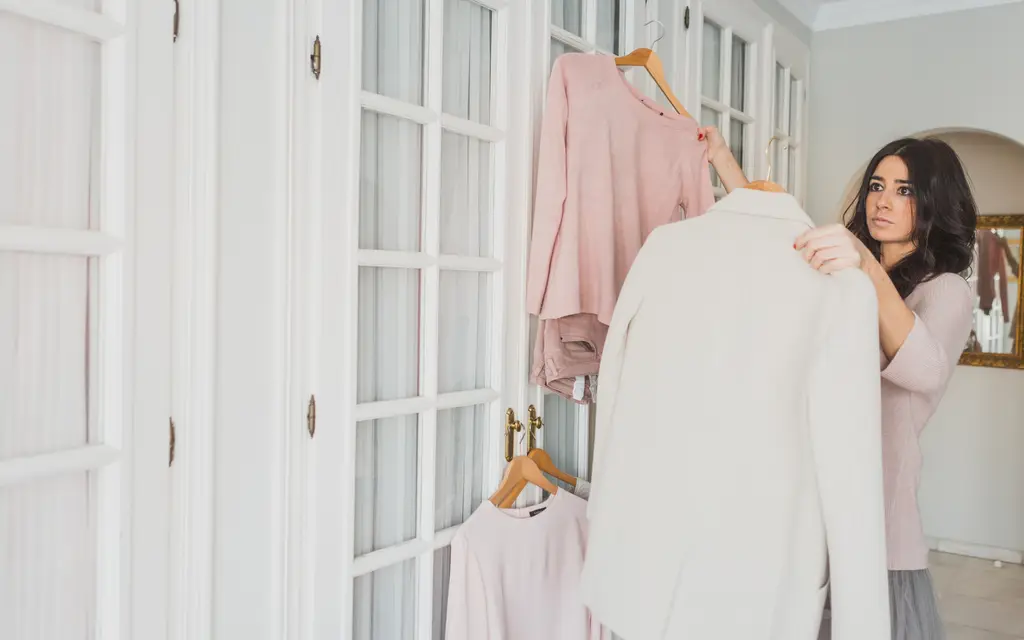 ハンガーにかけた2着の服を見比べて迷う人（イメージ写真）