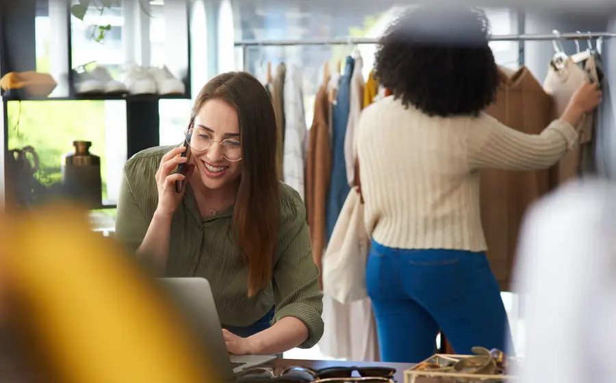 A shop assistant on the phone among the rails in a clothing store (illustrative photo)