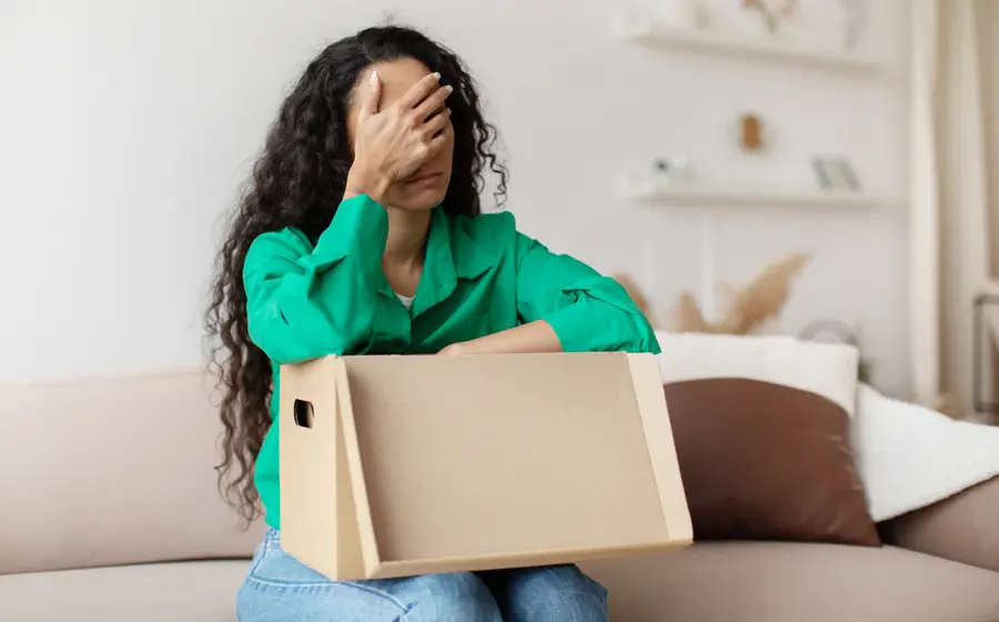 A buyer at home with an opened parcel, disappointed by what arrived (illustrative photo)